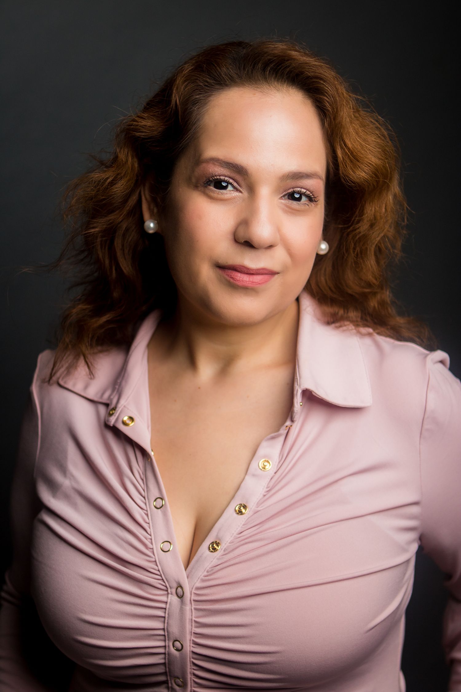 Professional portrait of a person in pink buttoned top with wavy auburn hair.