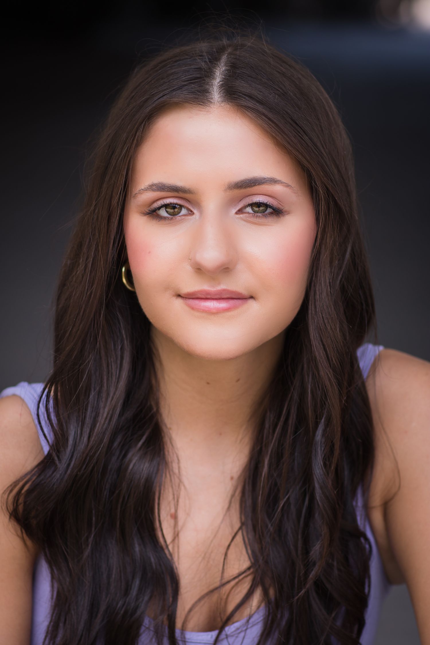 Professional headshot portrait of a young woman in a purple top with long dark hair and natural makeup.