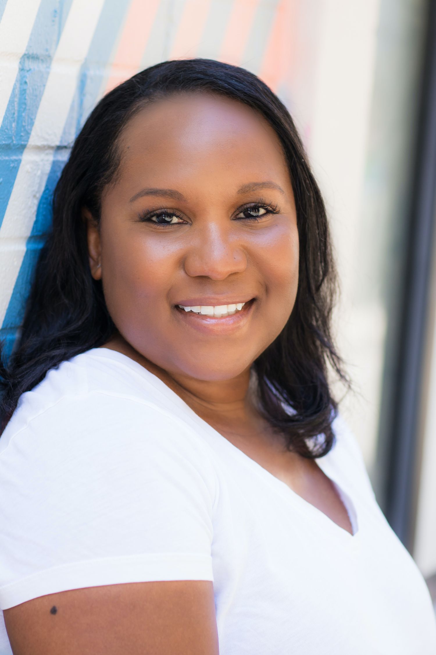Professional headshot of a woman in a white v-neck top with a bright smile against a colorful background.