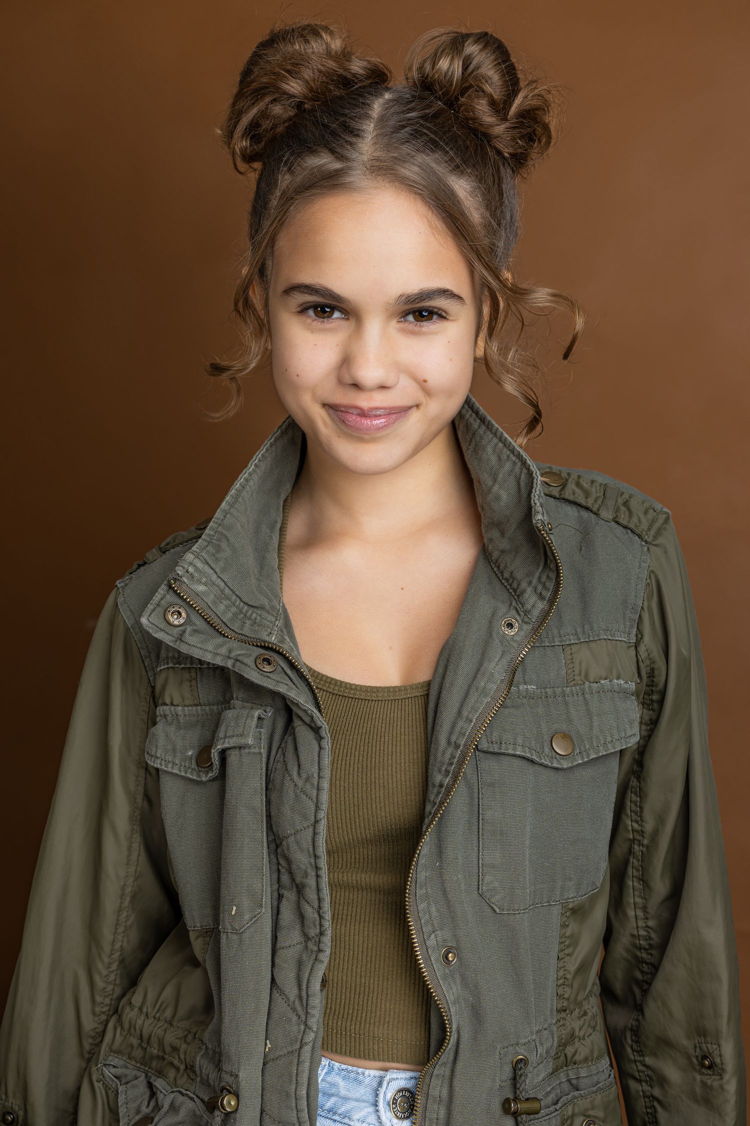 A sequence of casual portrait shots featuring someone in an olive military jacket and grey top against a brown backdrop.