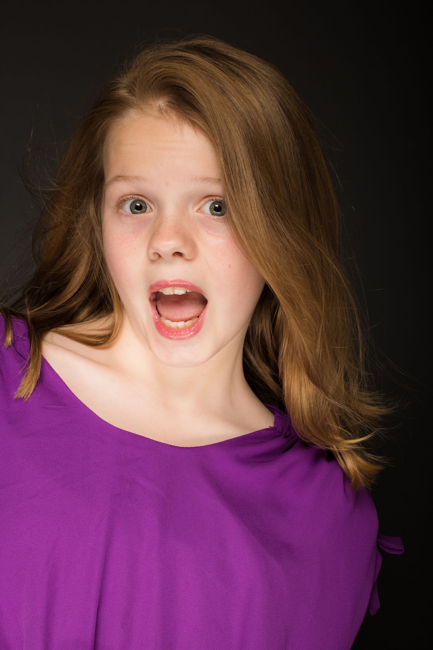 Expressive portrait in purple top against dark background.