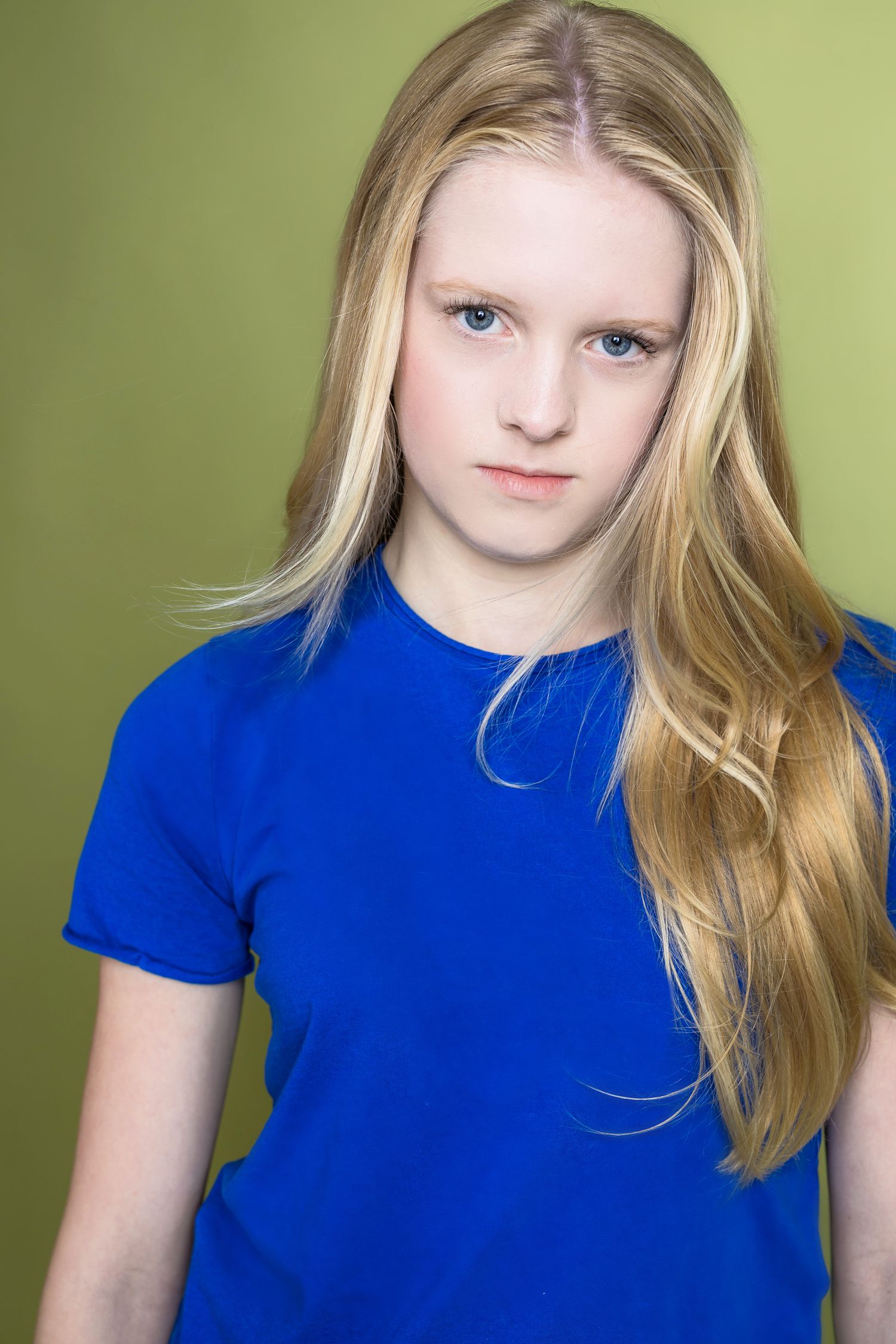 A portrait against a green background shows bright blonde hair and a vibrant royal blue t-shirt.