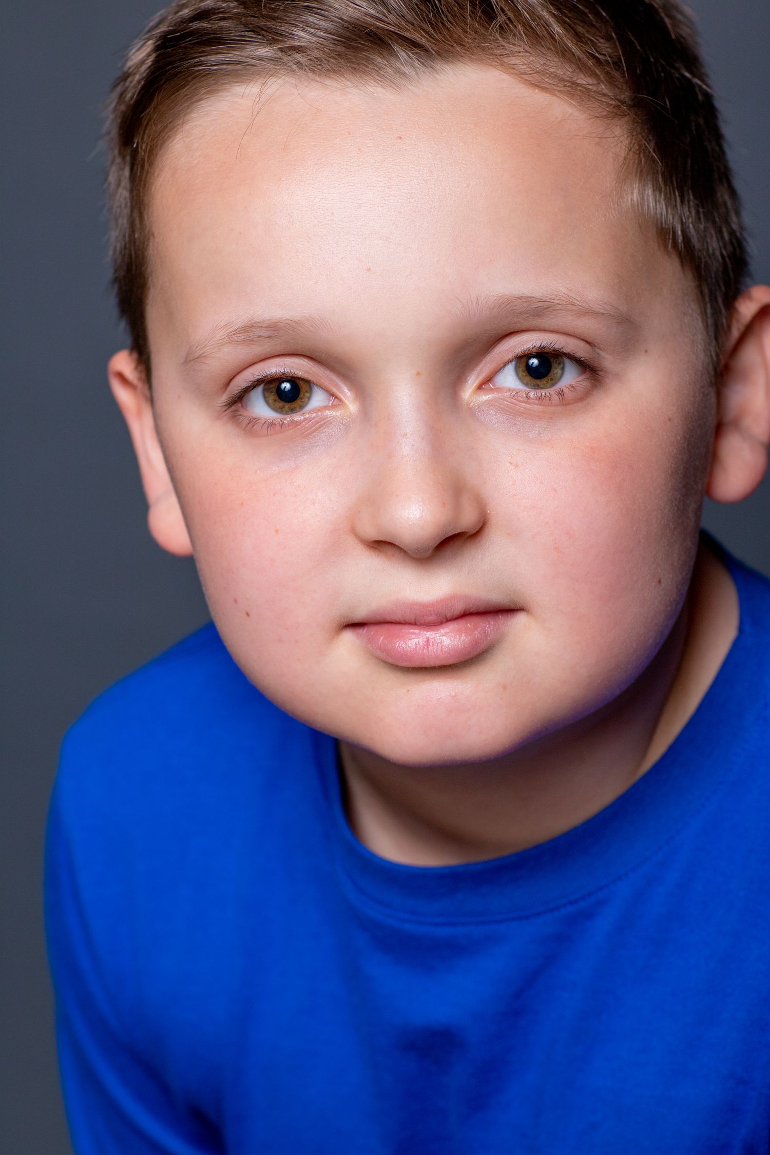 Close-up studio portrait of a young person in a blue shirt against a dark background.
