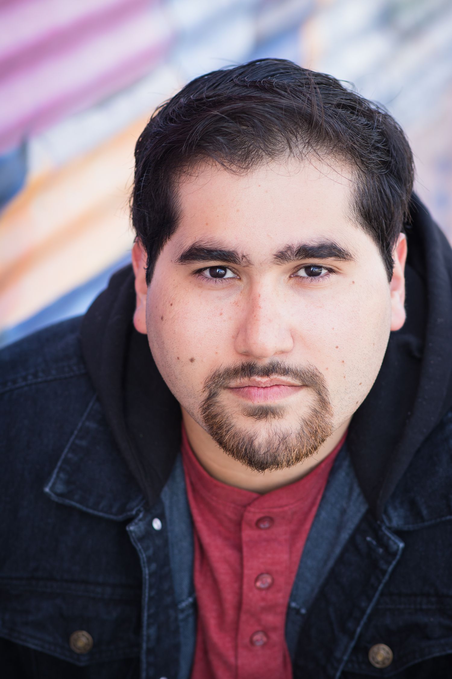 Professional portrait of a person in red henley and dark jacket against colorful background.