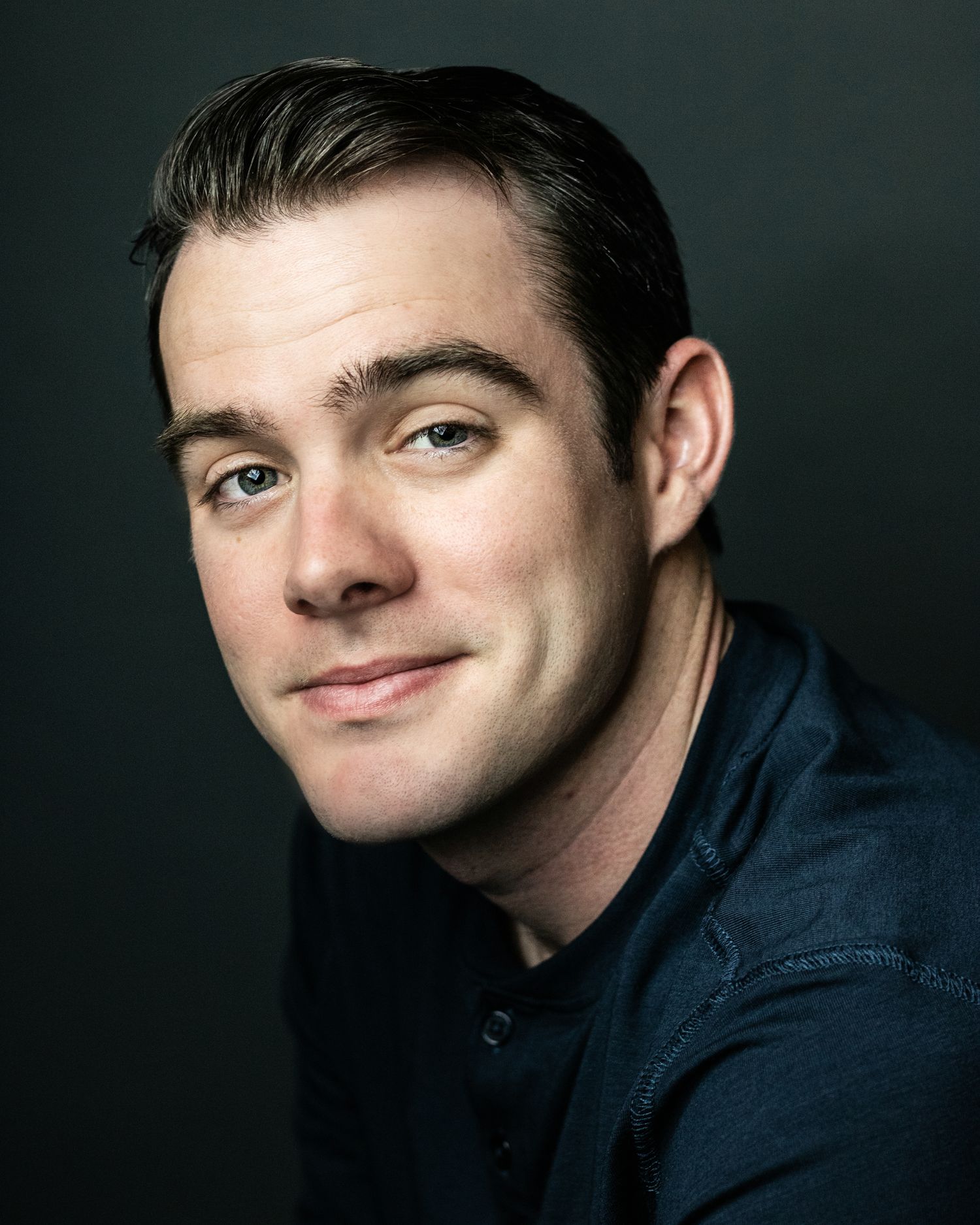 Studio portrait of a person in a navy jacket with a gentle smile against a dark background.