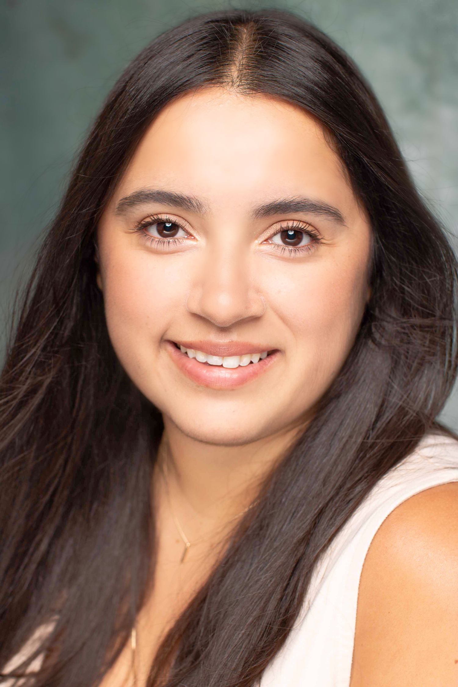 Professional headshot of a woman with long dark hair and natural makeup wearing a white top.