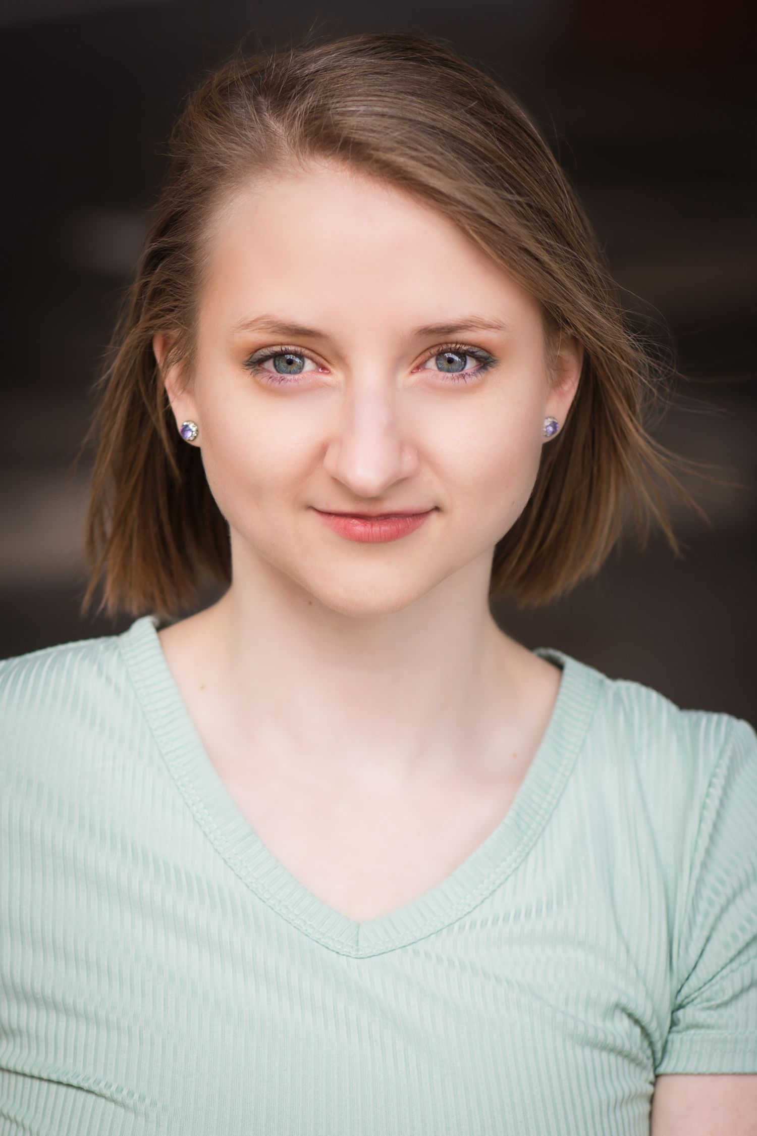 Professional headshot of a person in mint green top with short brown hair against dark background.