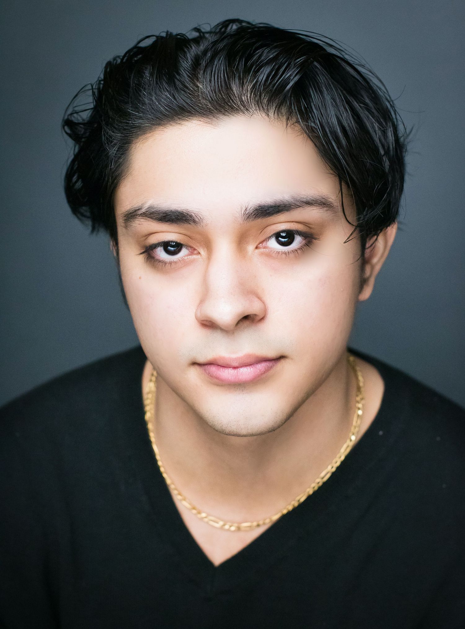 Professional studio portrait of a person wearing a black v-neck and gold chain necklace.