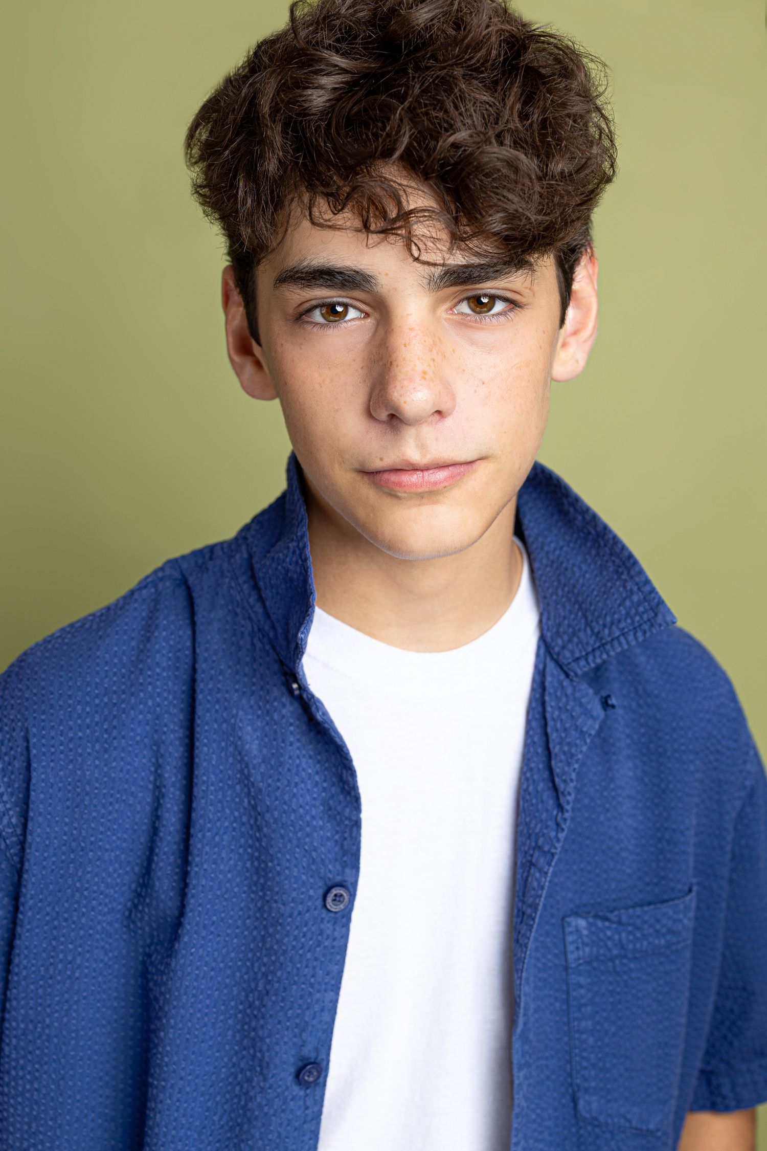Portrait of someone wearing a blue button-up shirt and white t-shirt against a green background.