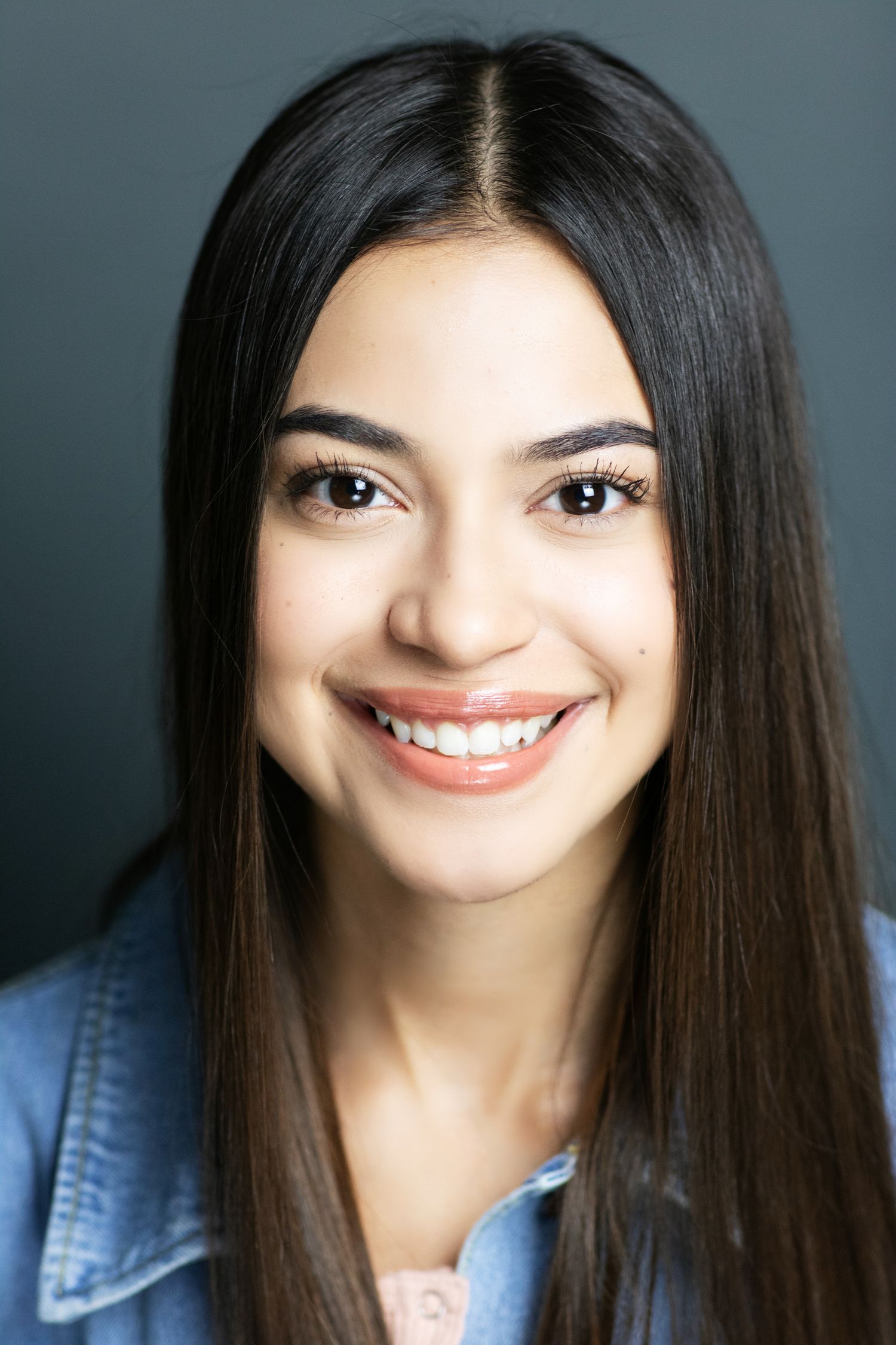Professional headshot of a woman with long dark hair wearing denim and smiling at camera.