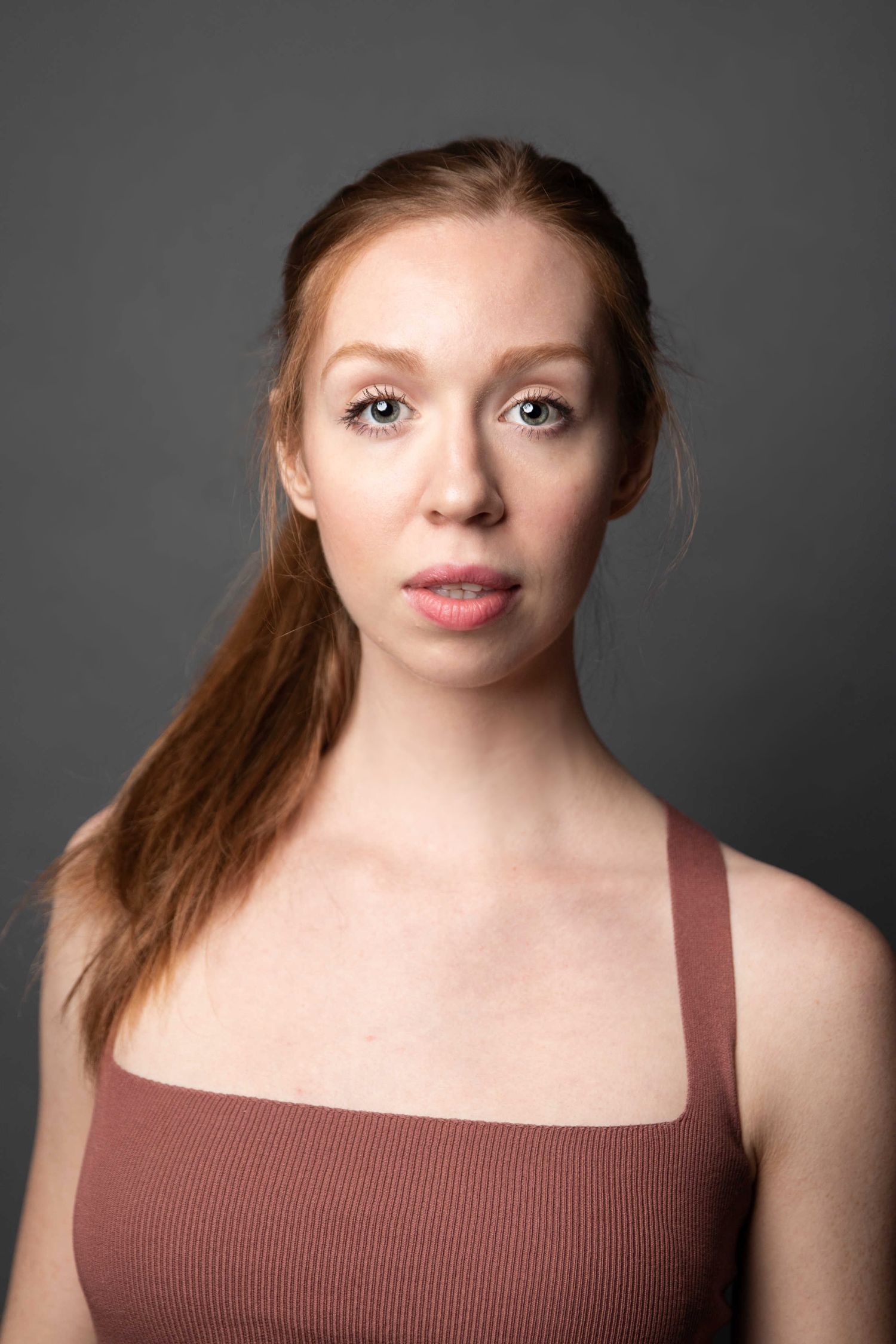Studio portrait of a person in a brown top against a dark gray background.