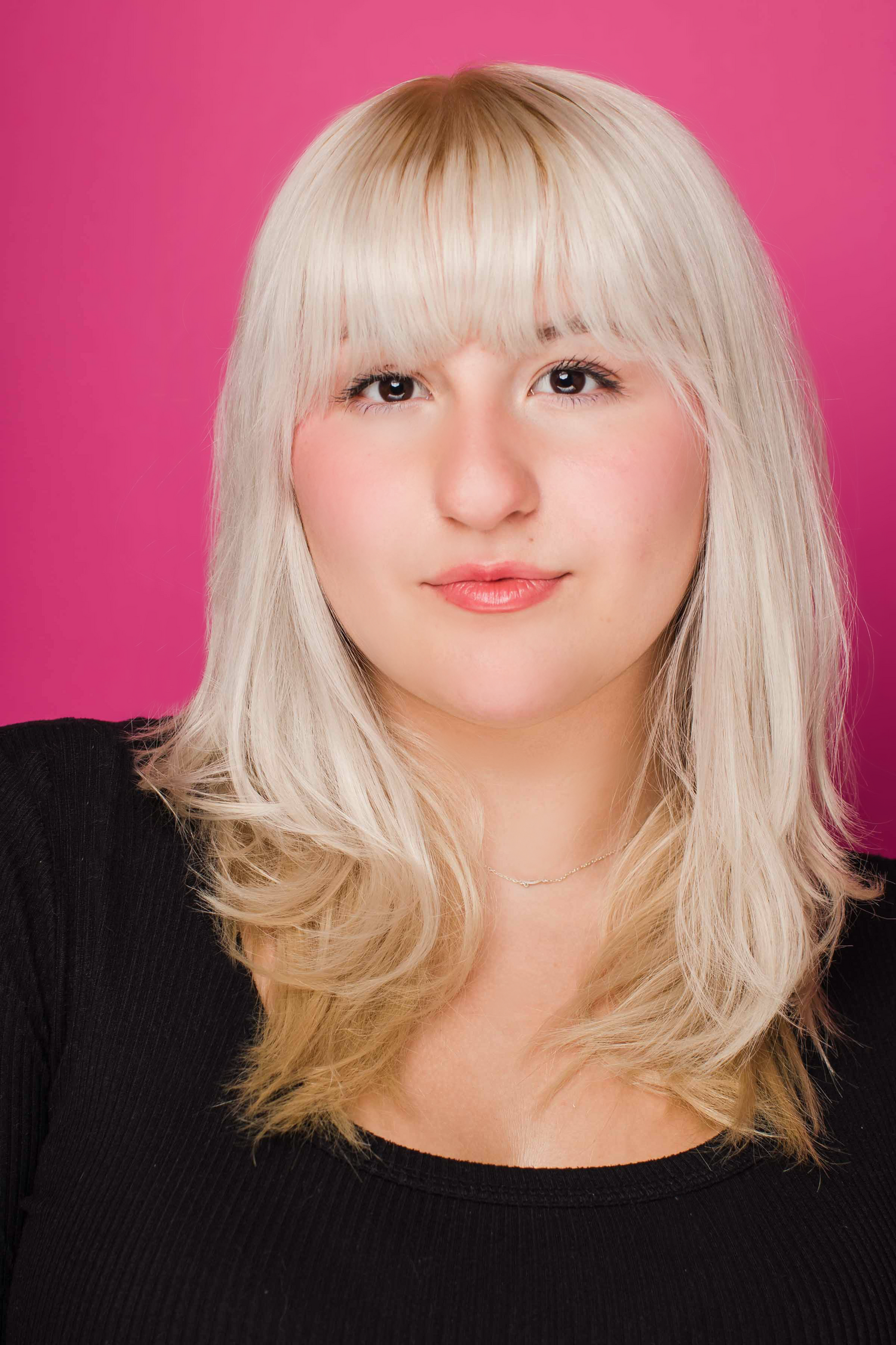 Professional headshot of a young woman with platinum blonde hair against a pink background.