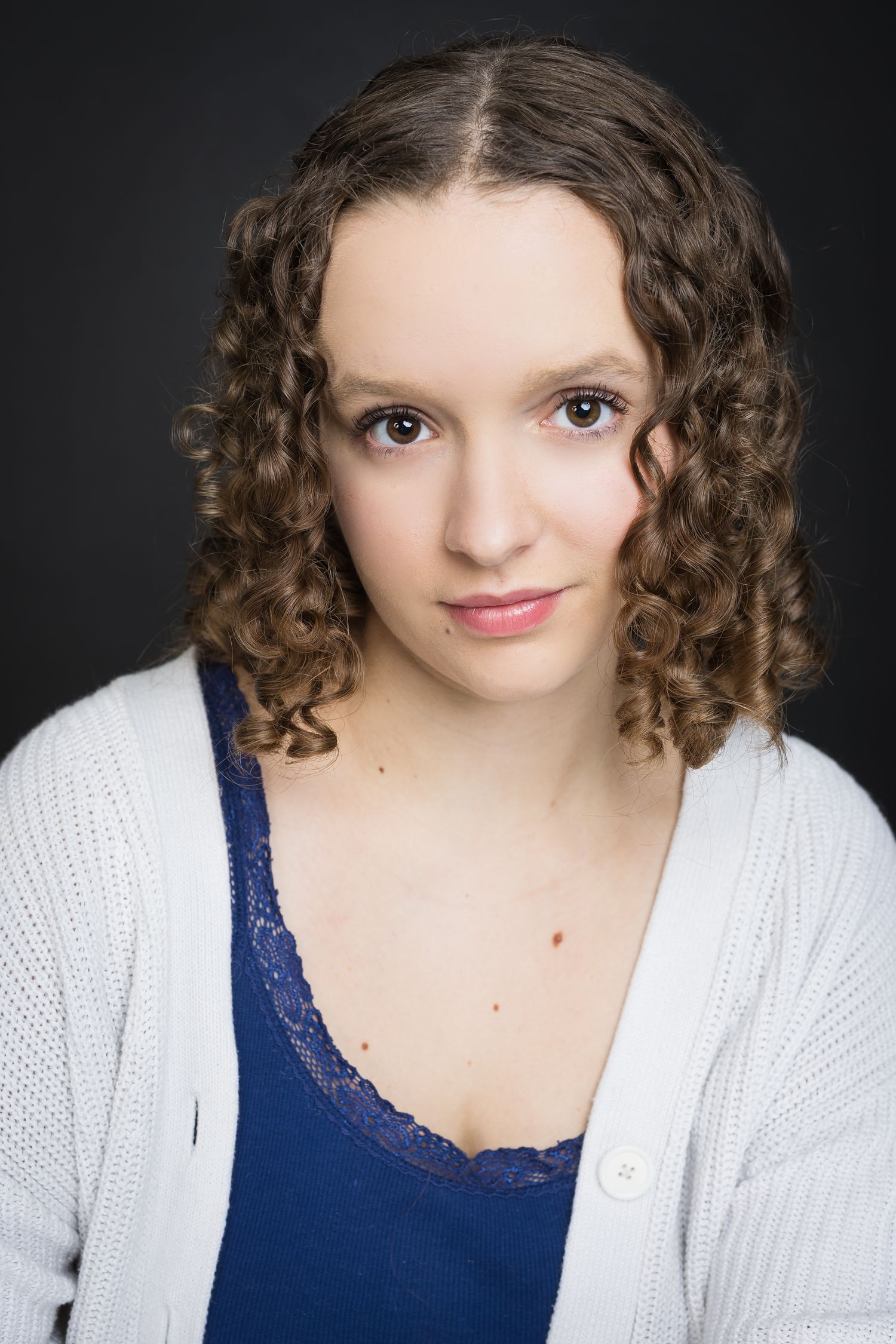 Portrait series against dark background showcasing curly hair and white cardigan with navy top.