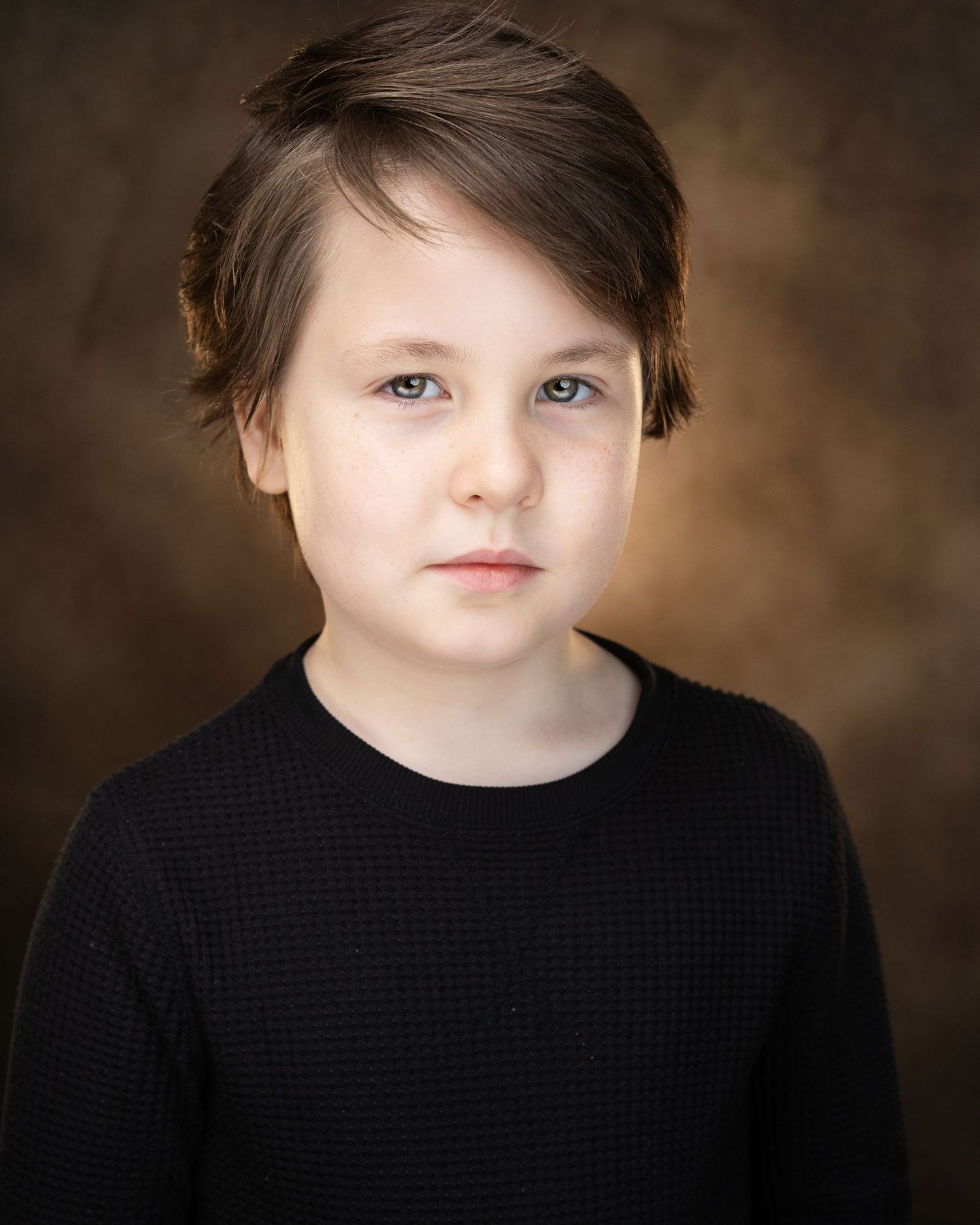 Young boy with brown hair and blue eyes wearing a black sweater, posed for a professional portrait photo.