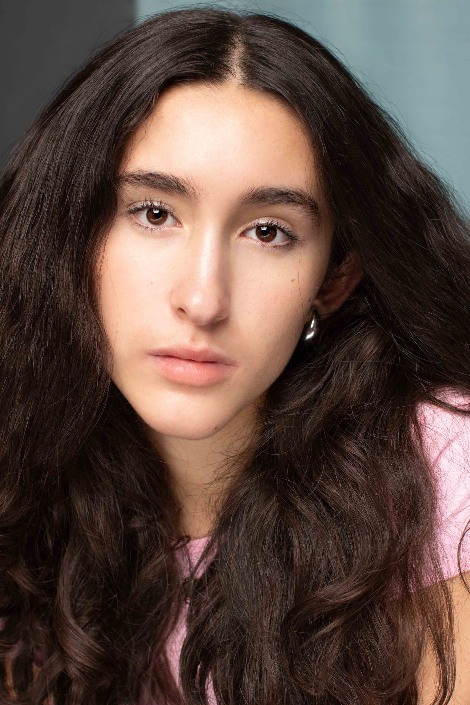 Studio portrait of a woman with long dark hair wearing a pink top against a muted background.