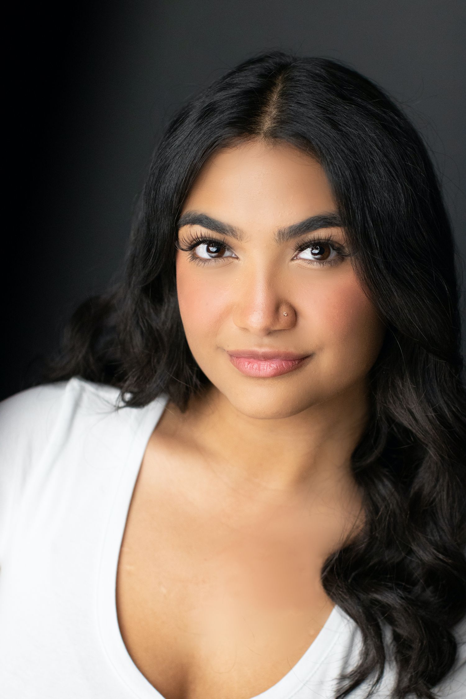 Professional headshot of a woman in white against dark background with long black hair and natural makeup.