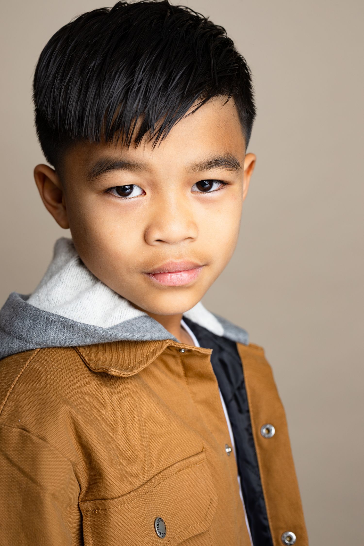 A young child wearing a brown coat with a gray collar poses in a series of close-up portrait shots.