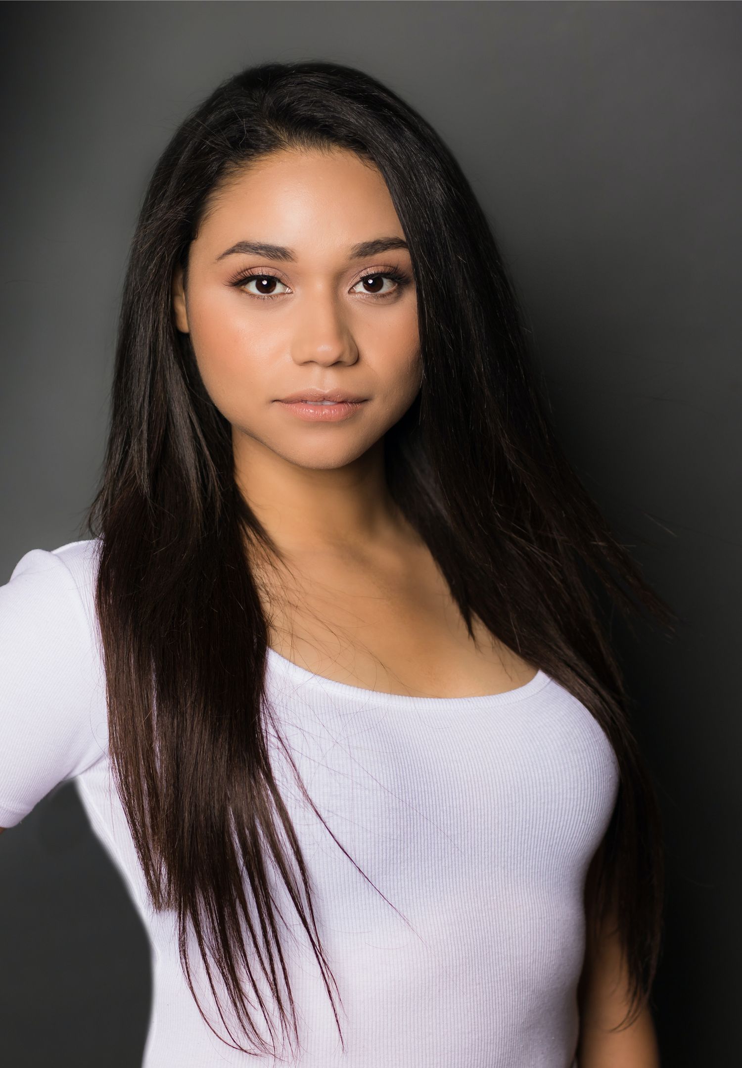 Professional studio portrait of a woman in white top with long straight dark hair.