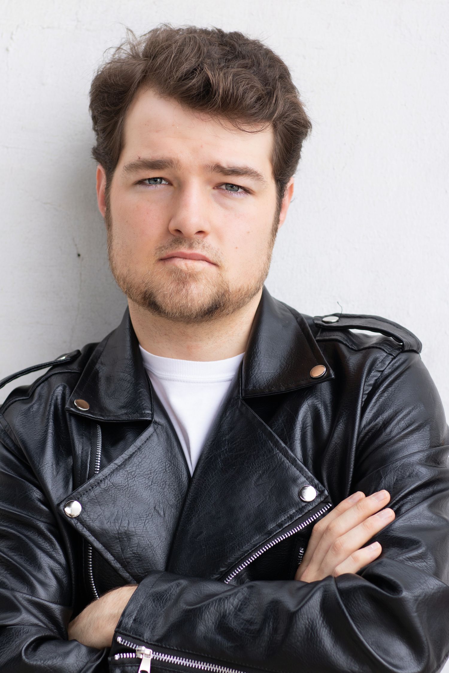 Portrait of a person in a leather jacket with crossed arms against a white background.