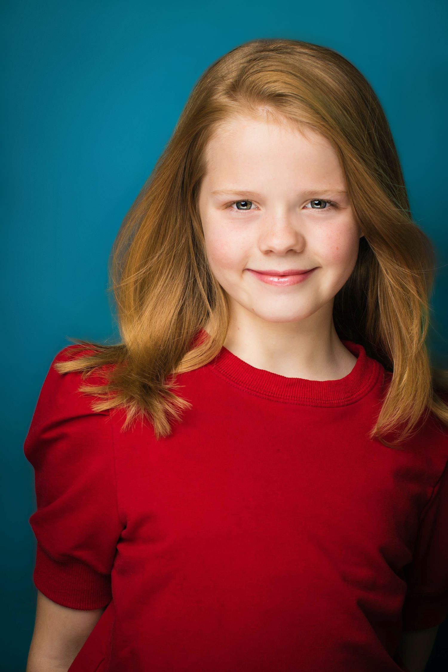 Portrait of a young girl in a red shirt against a turquoise background.