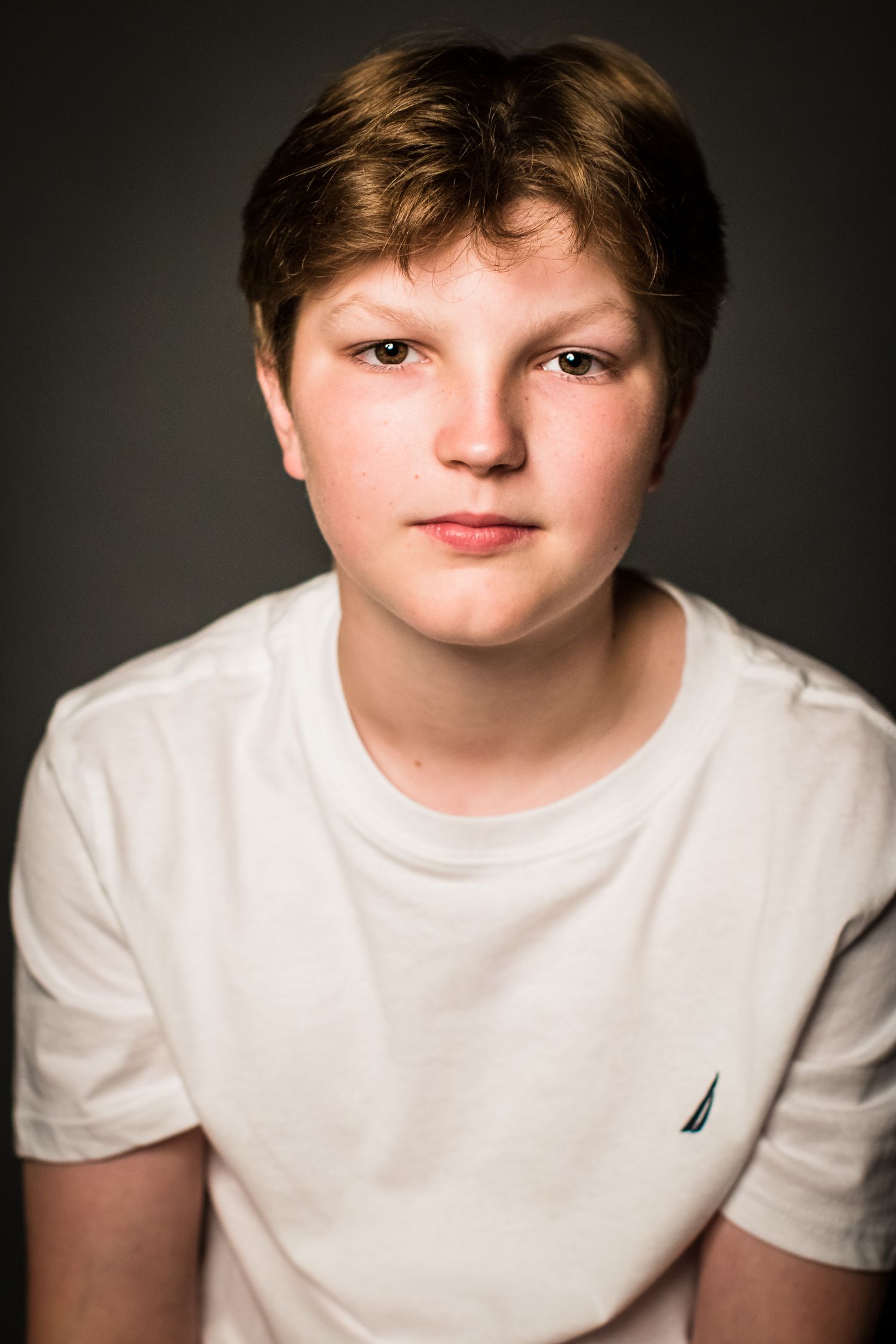Studio portrait of a youth in a white t-shirt with short brown hair against a dark backdrop.