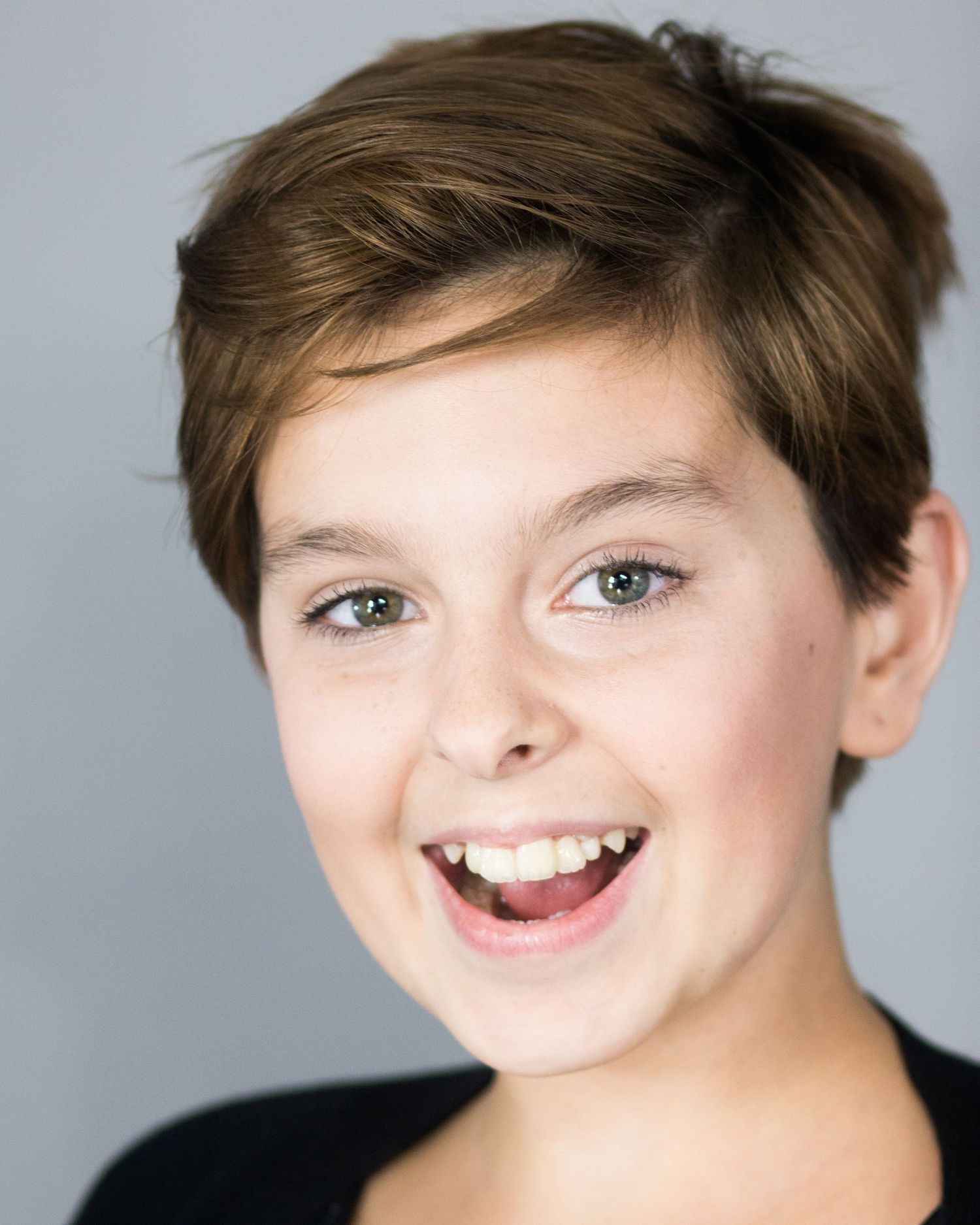 Close-up headshot of a young person with a bright smile against a gray background.