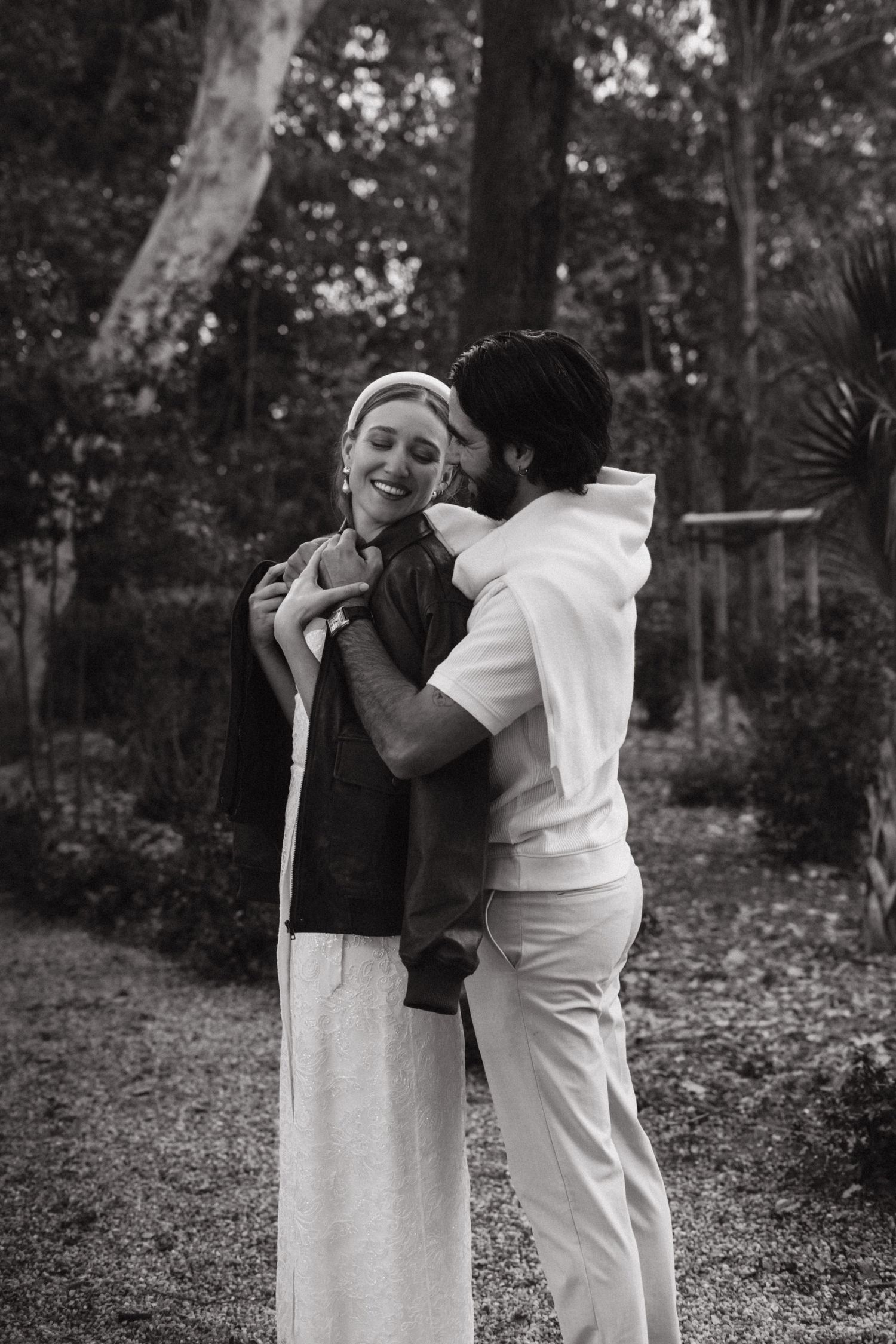 Black and white portrait of a couple embracing in a wooded garden setting.