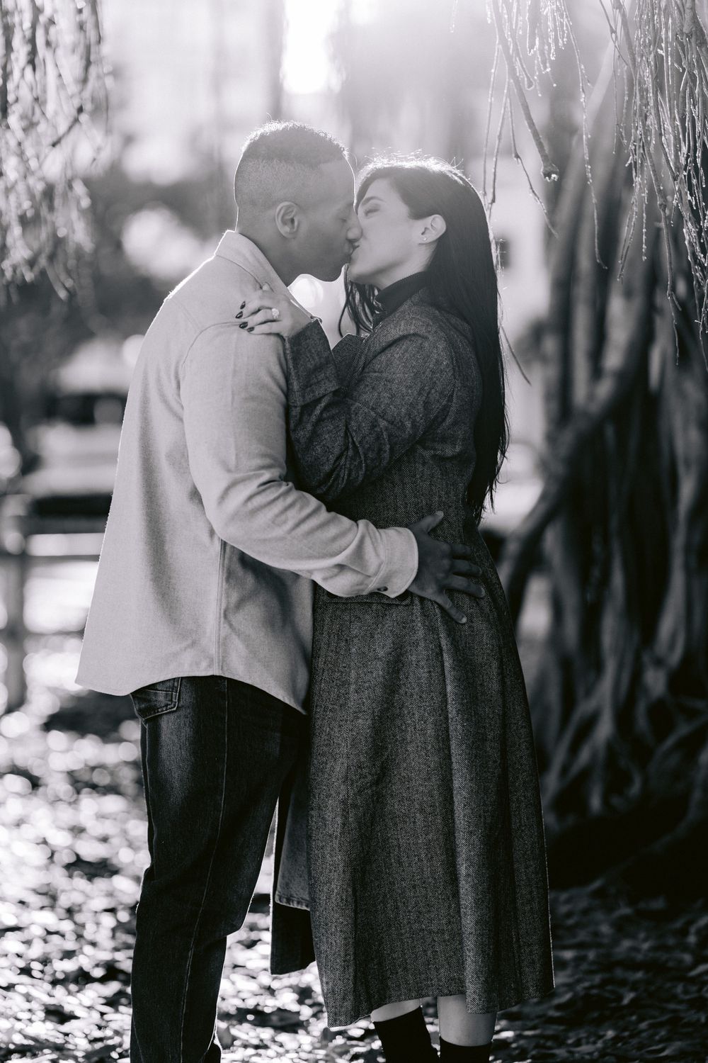 A romantic black and white portrait of a couple sharing an intimate kiss in a winter forest setting.