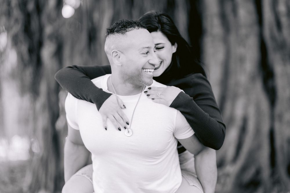 A joyful couple shares a playful piggyback ride moment in black and white photography.