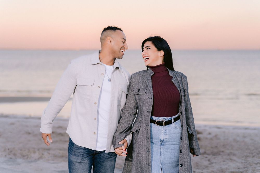 A couple holds hands and shares a romantic moment while walking on the beach at sunset.