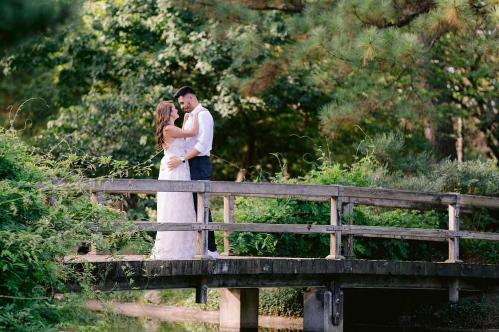 Romantic couple sharing a tender moment on a wooden bridge surrounded by green foliage.