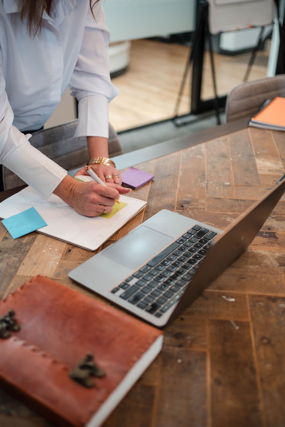 Close-up of hands taking notes beside laptop keyboard on rustic wooden desk in white sleeves.