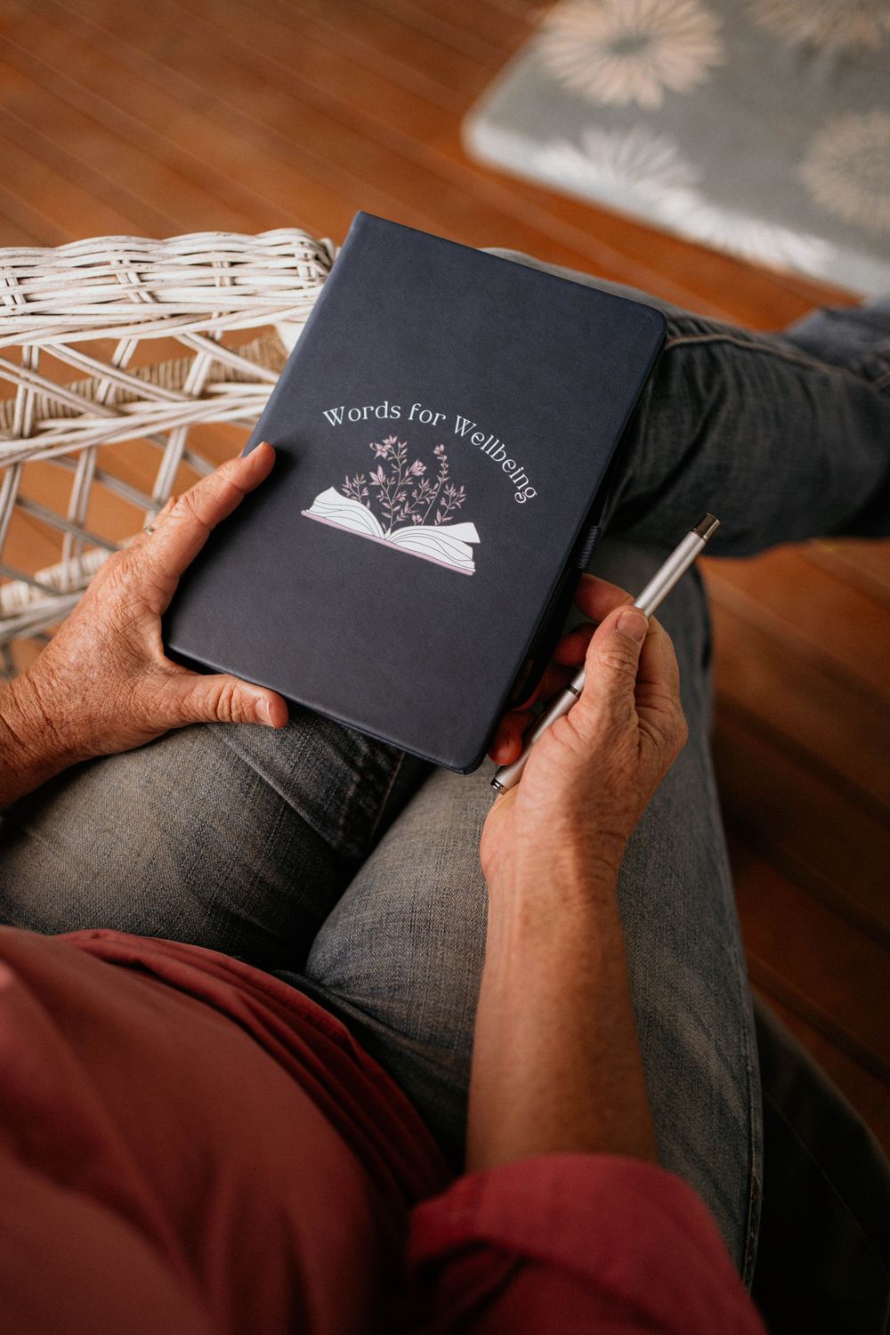 Hands holding a black notebook with decorative mountain illustration while sitting on hardwood floor.