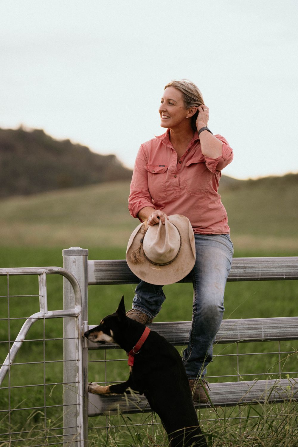 A person and their black dog spending time outdoors by a wooden fence in the countryside.
