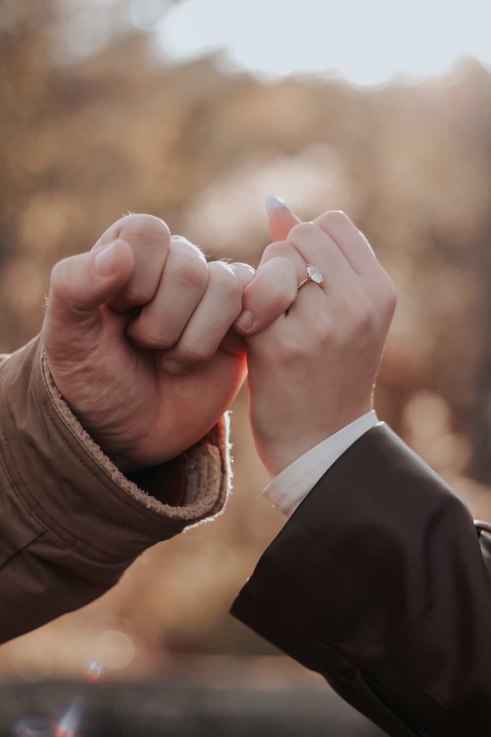 Close-up of two hands making a pinky promise against a sunset background.