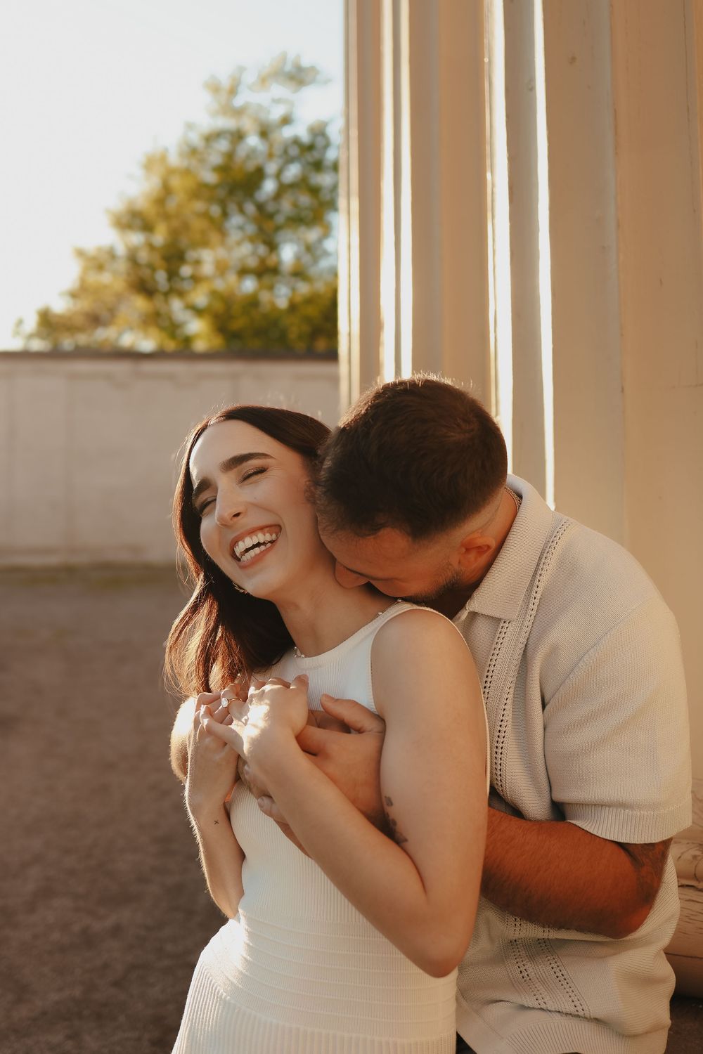 Romantic couple shares intimate moments together on a bright porch with sun-filled background and light rustic tones.