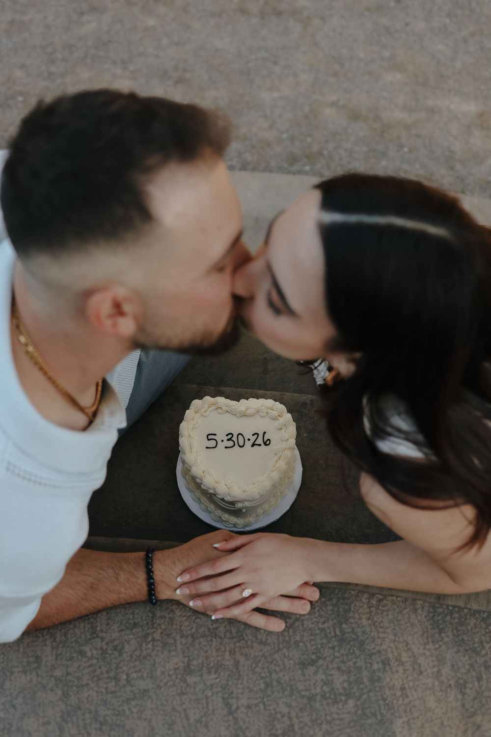 A romantic save the date photo features a couple kissing with a small white cake displaying the date 5.30.24.