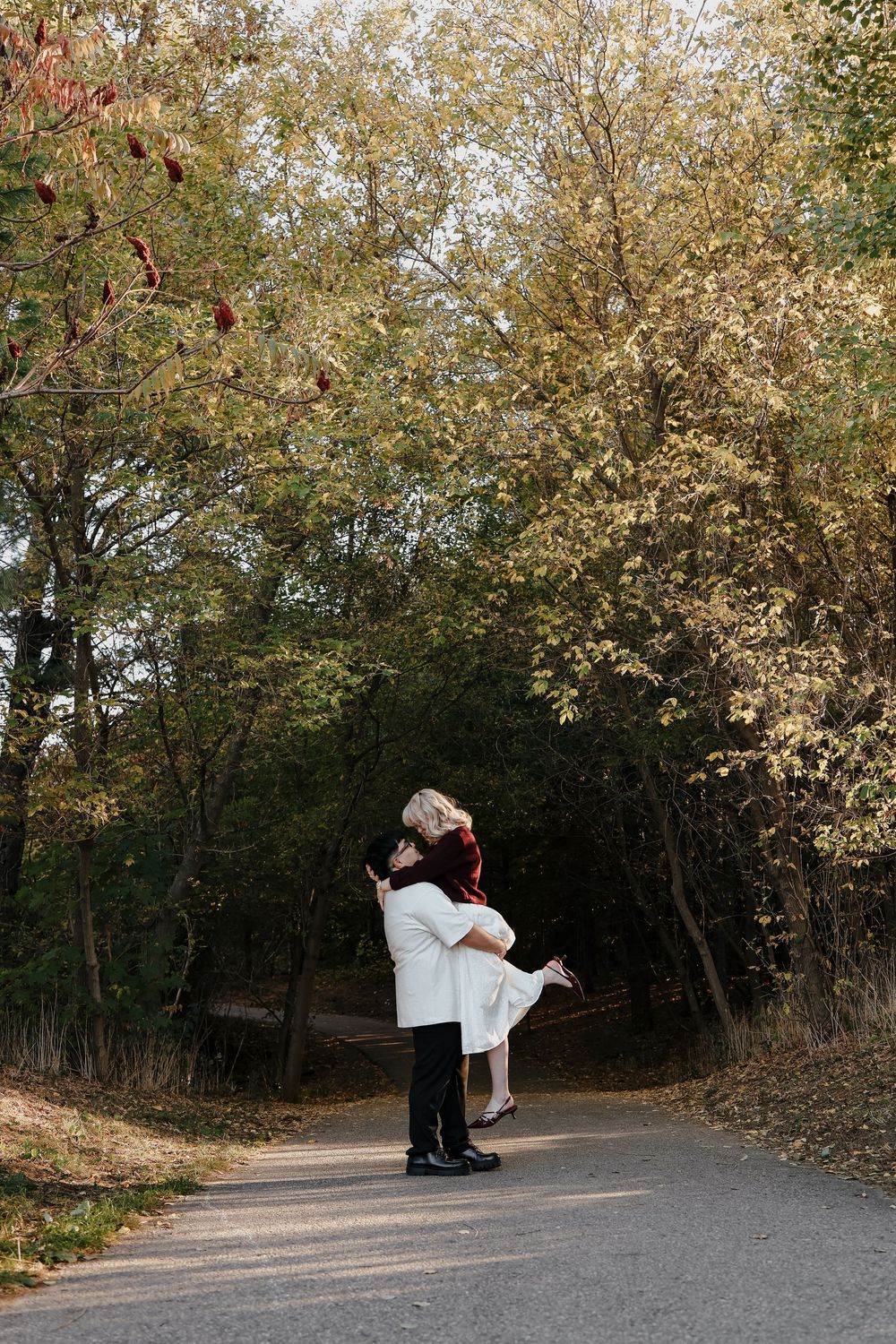 A series of four images showing a couple dancing and performing lifts on a scenic autumn path surrounded by trees.