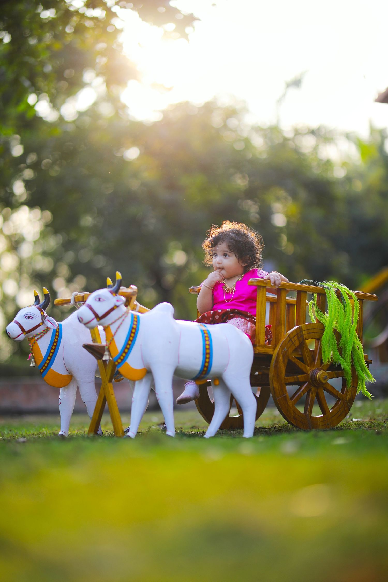 Toy chariot with white horses and small child in bright pink dress in garden setting.