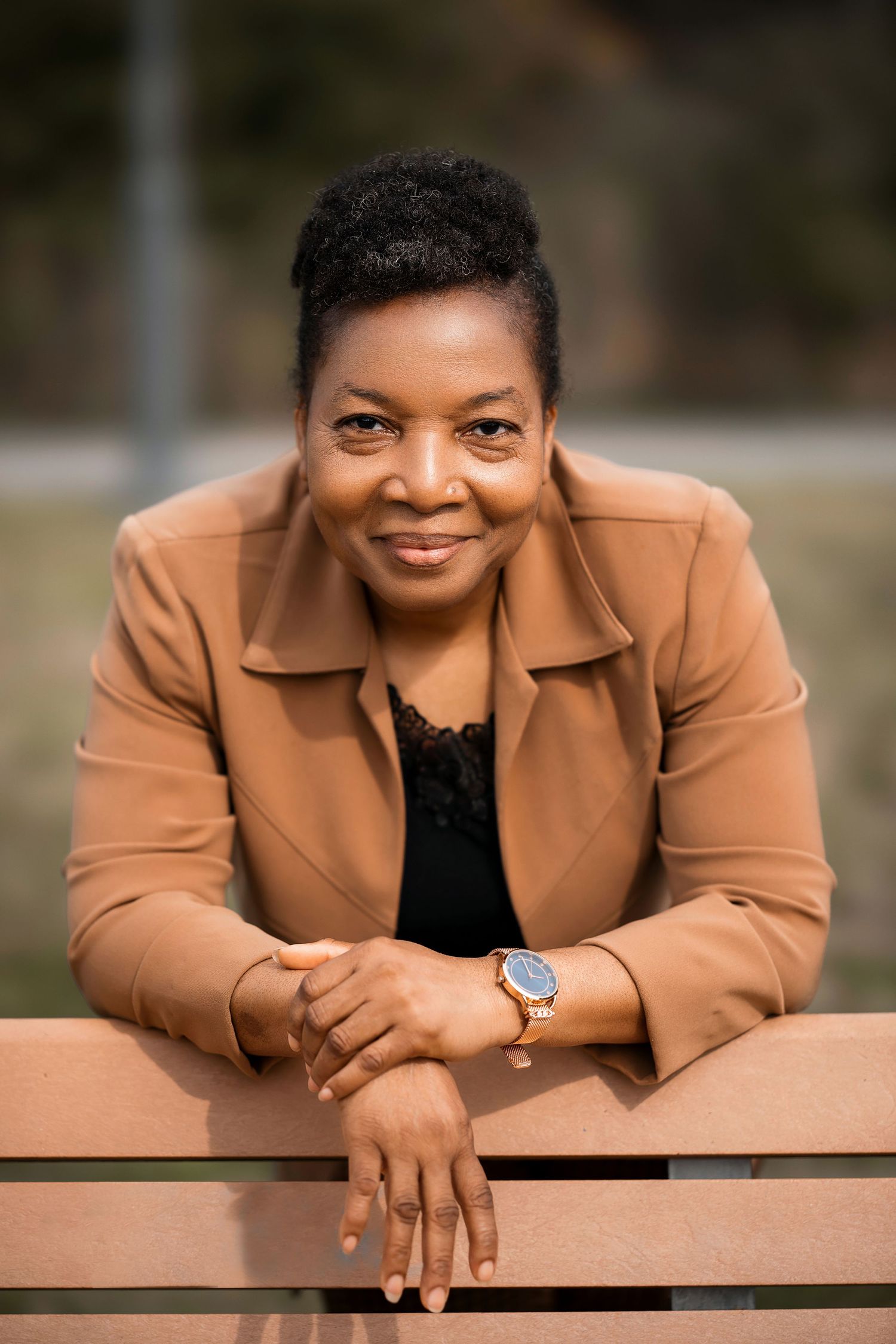 Professional outdoor portrait in tan blazer leaning on wooden bench.