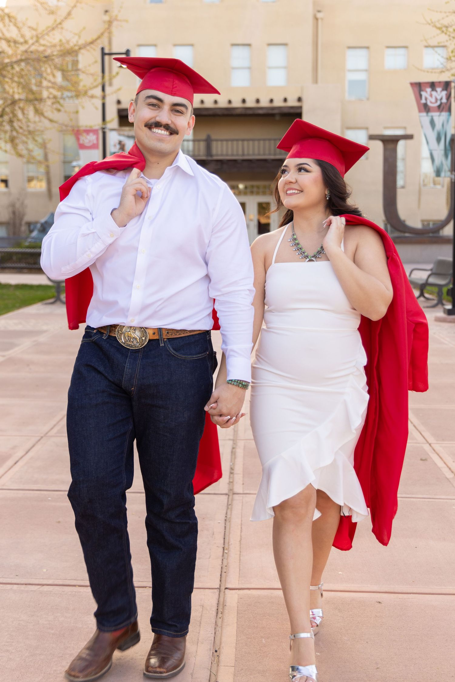 Graduates in red caps and gowns pose together on campus wearing white and denim.