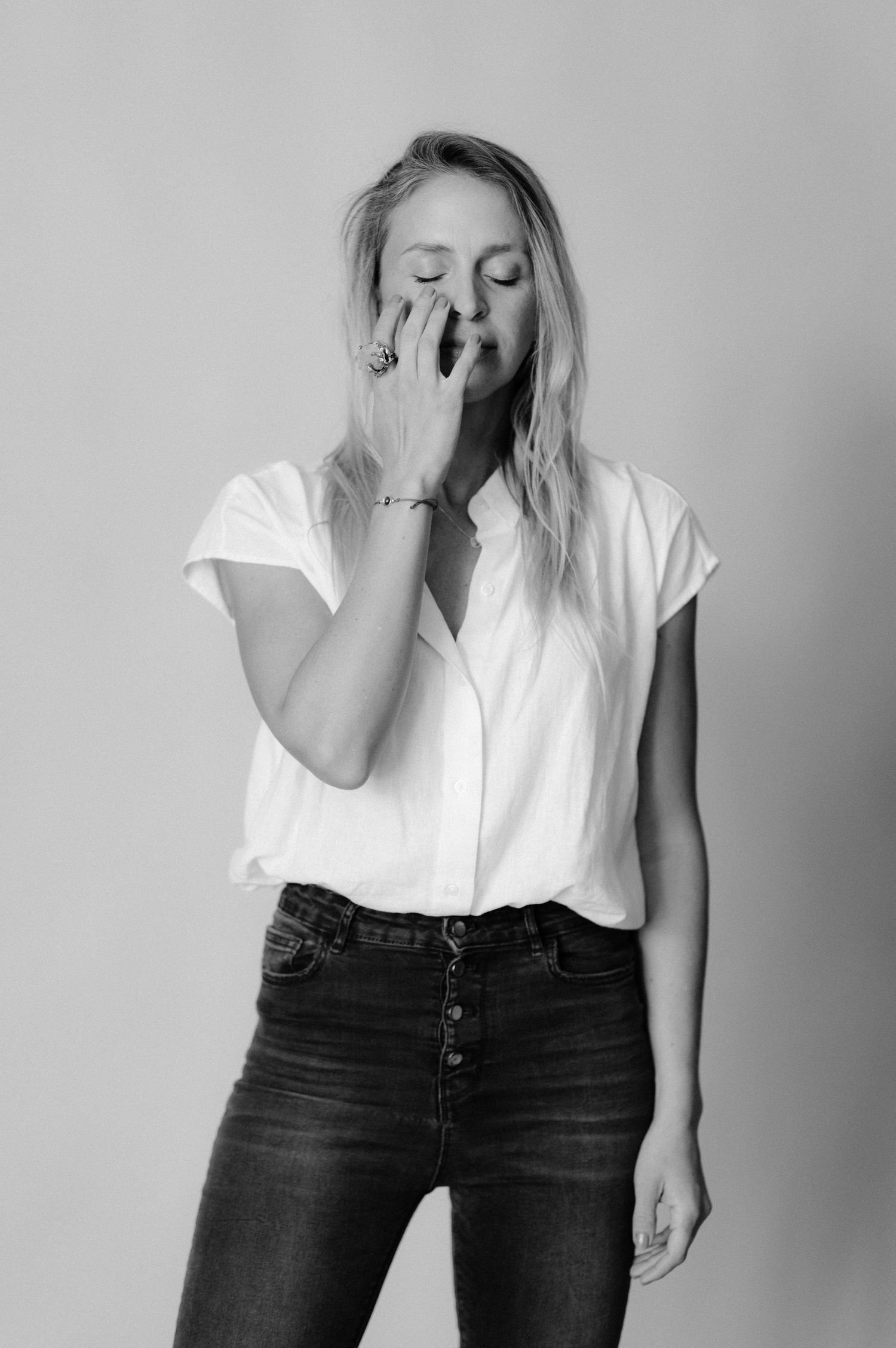 Monochrome portrait of person in white top and jeans with hand gesture near face.