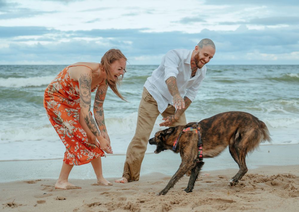 Couple playing with their dog on a cloudy beach at the ocean.