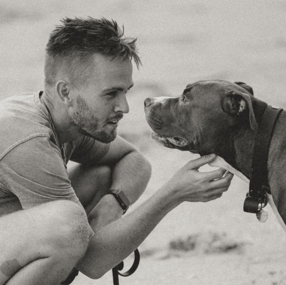 Person sharing intimate moment with brown dog on sandy beach in black and white.