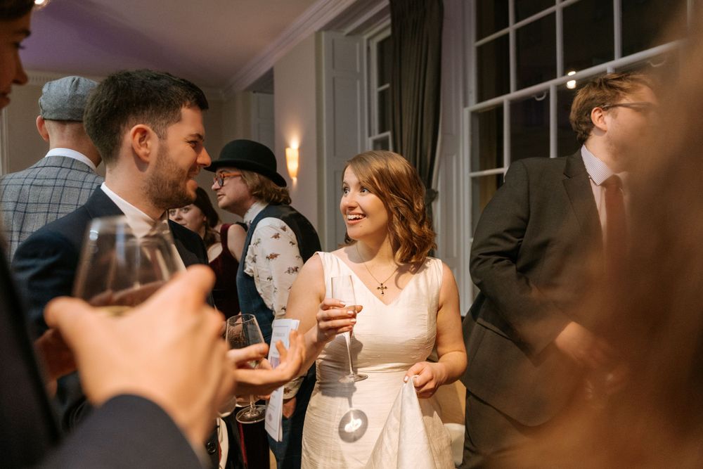 Wedding guests mingling and socializing with drinks at an indoor reception.