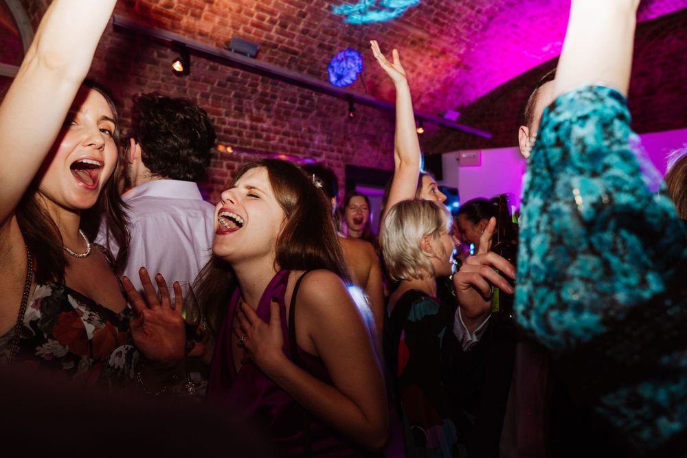 Enthusiastic party guests dancing and celebrating under colorful lights in a brick-walled venue.