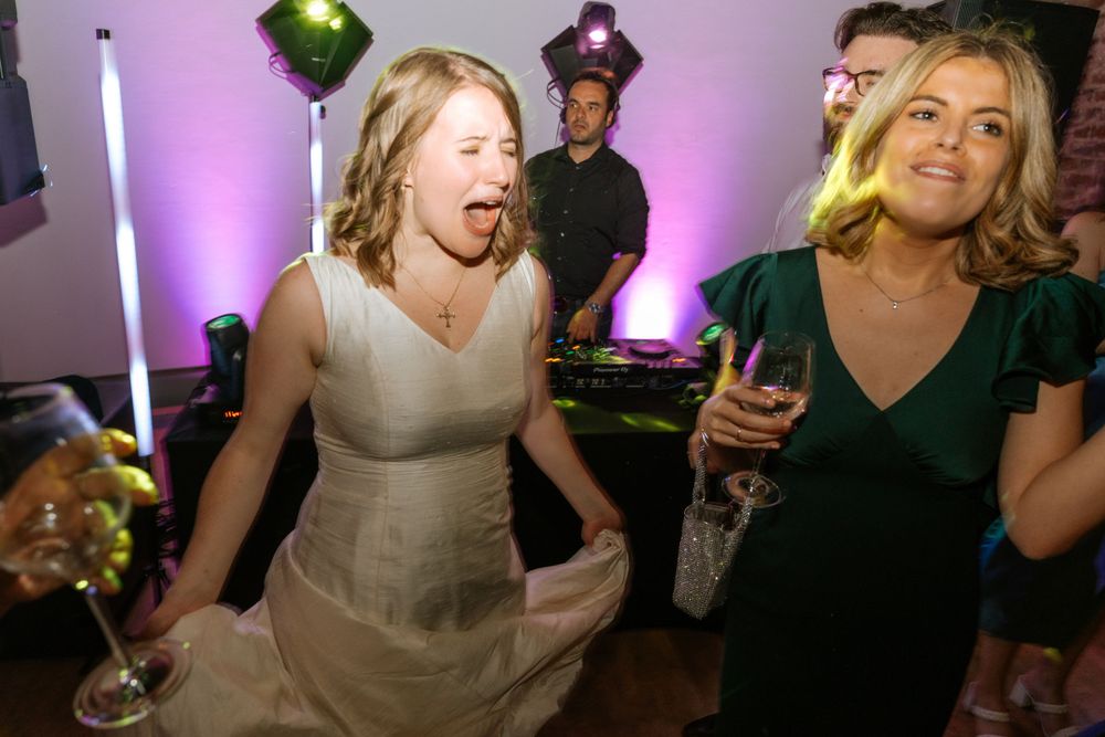 Wedding reception guests dancing and celebrating under purple mood lighting.