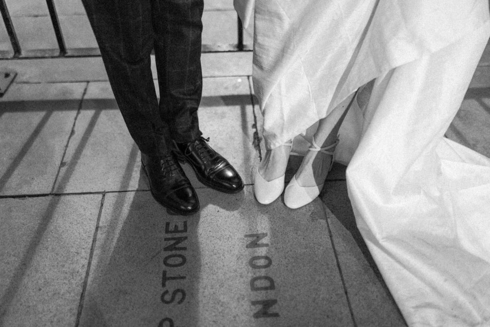Black and white detail shot of formal shoes and wedding dress hem on patterned floor.