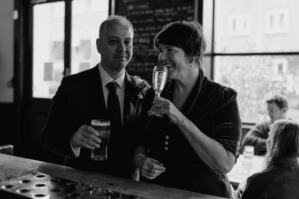 Two people share drinks and conversation at a pub counter.