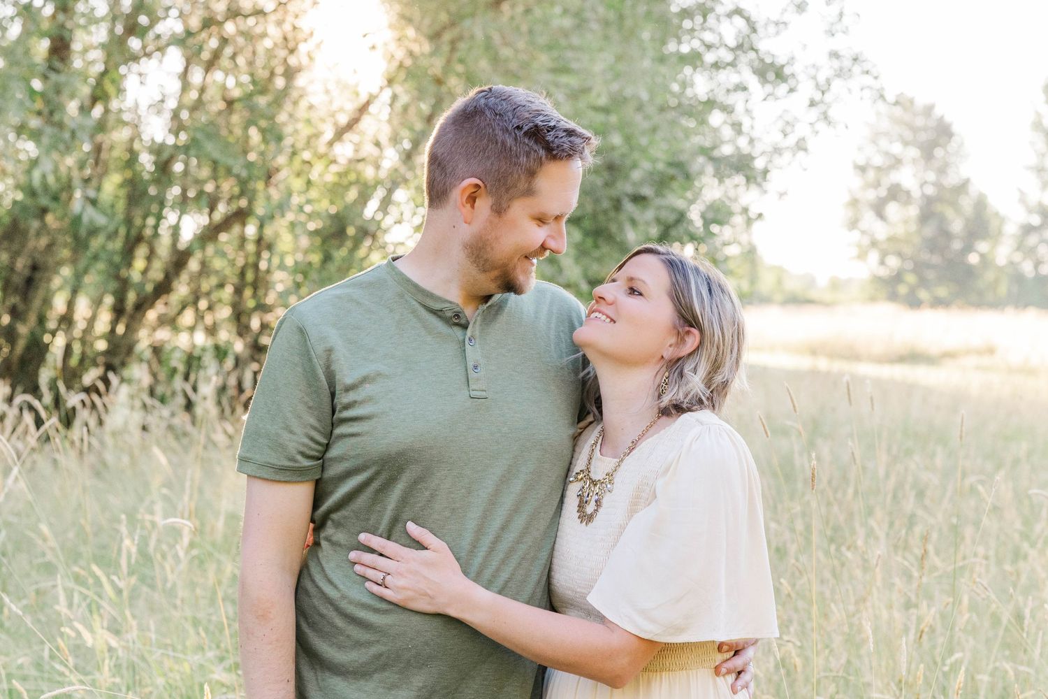 Smiling couple sharing a tender moment in a sunlit field of tall golden grass.